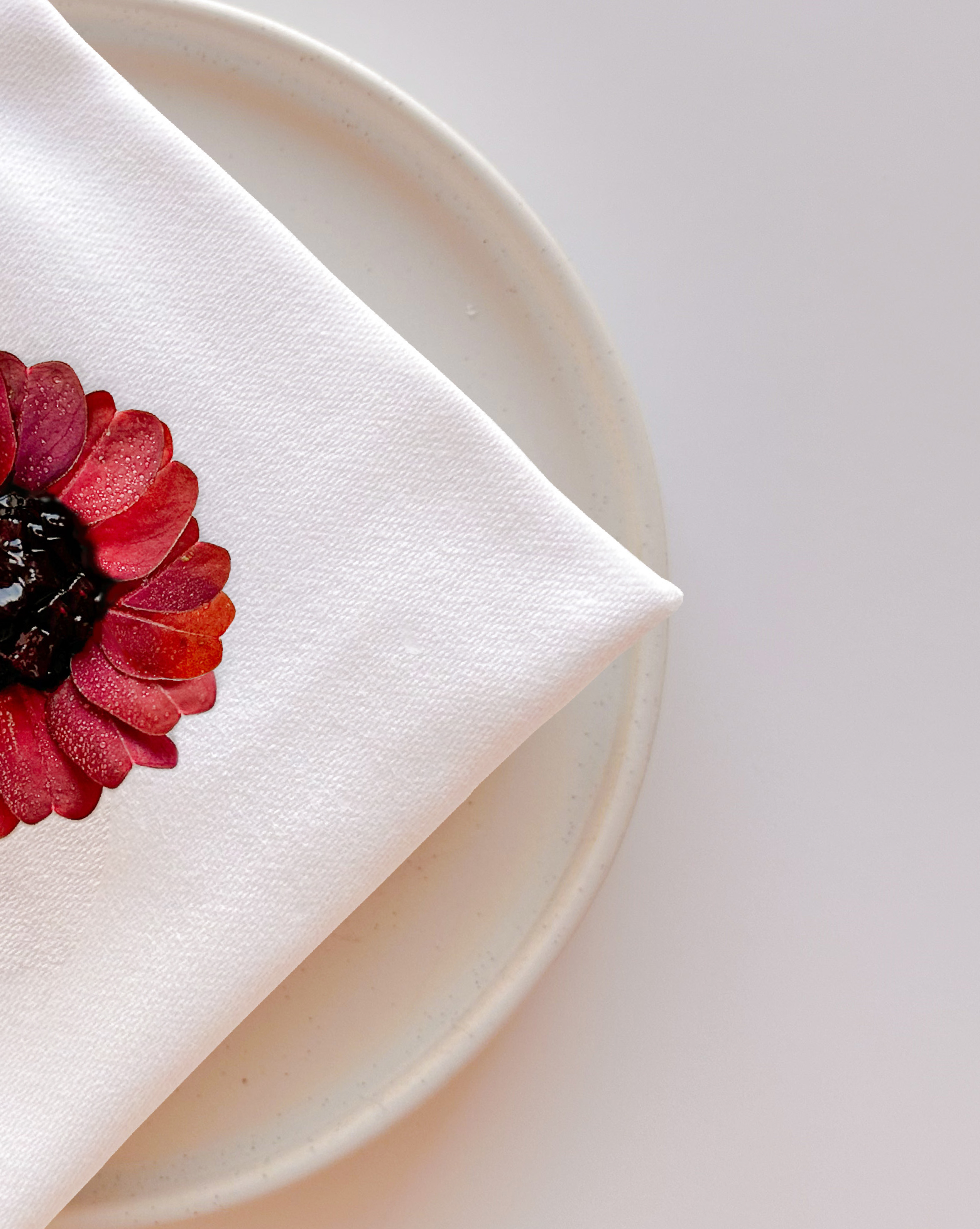A place setting, white linen and a flower on ceramic